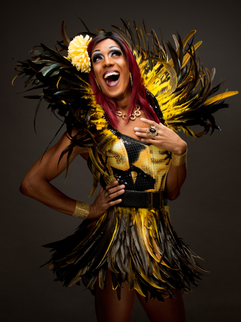 Smiling performer in a yellow-and-black feathered carnival outfit with a large yellow flower in her hair.
